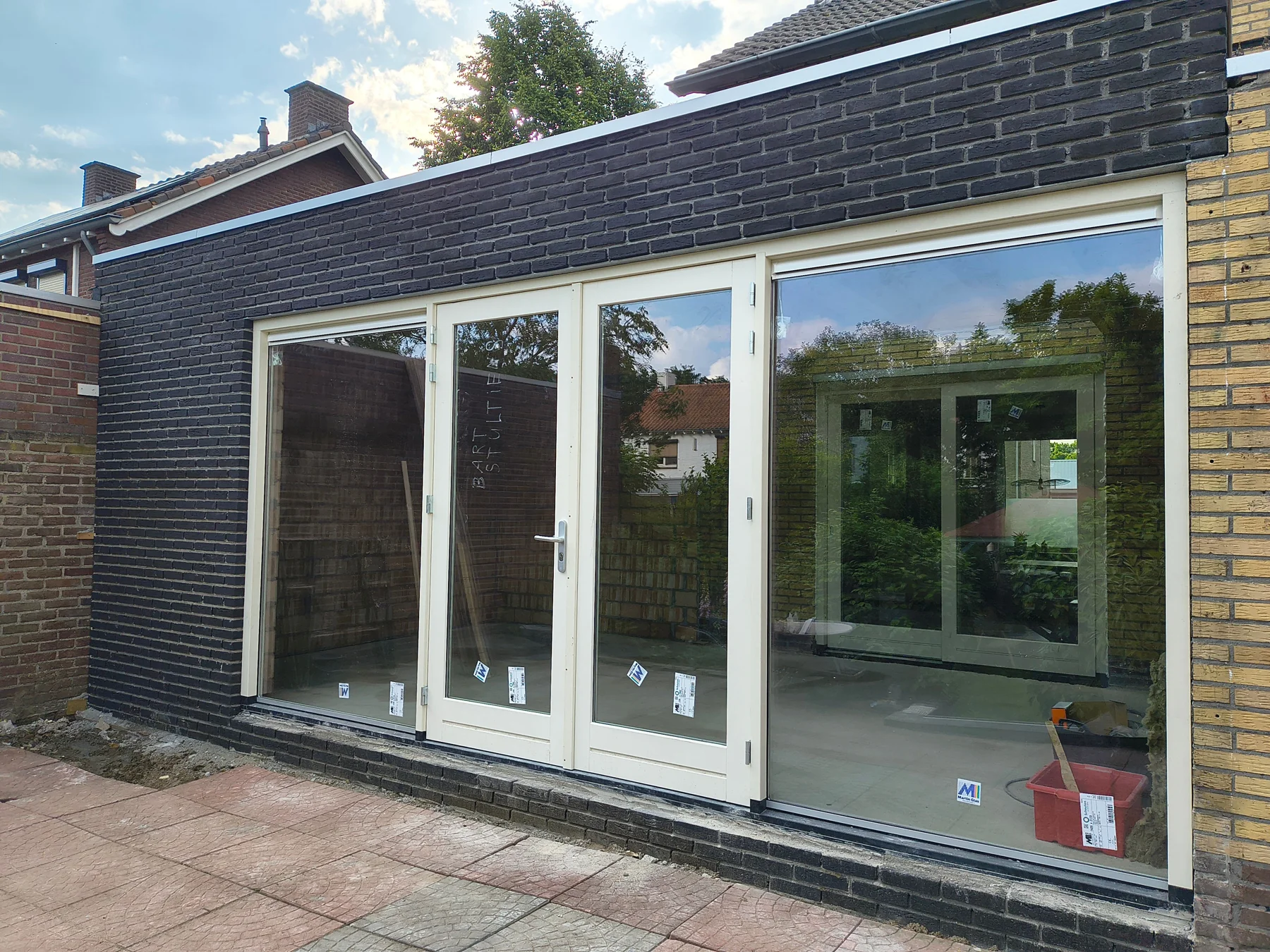 Aanbouw met donker metselwerk en witte glazen deuren